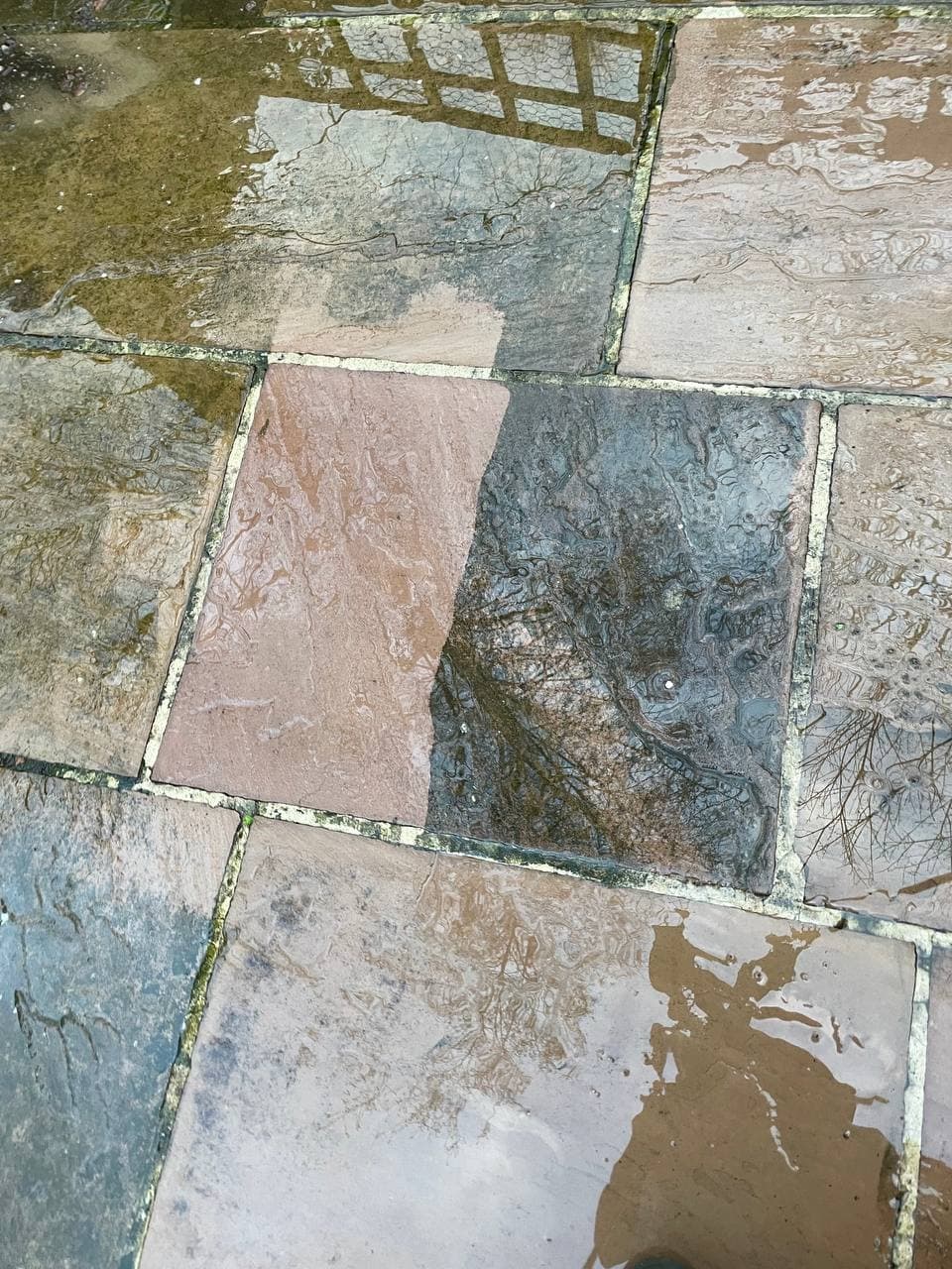 A flagstone half cleaned by jet washing, showing the difference against the dirty stone